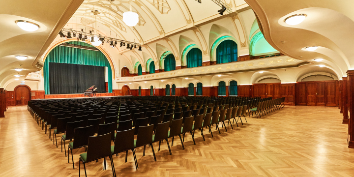 Diagonaler Blick in den Ernst-Abbe-Saal von einer Ecke des Raums auf die Bestuhlung und die Bühne, oberhalb ist die Trobüne zu sehen.  ©JenaKultur, Karoline Krampitz