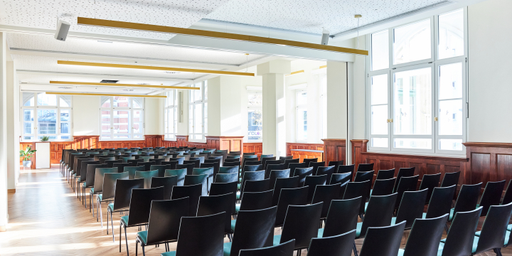 Sonnendurchfluteter Grete-Unrein-Raum im Volkshaus Jena mit einer Bankettbestuhlung, Fensterreihe und Säulen auf der rechten Seite.